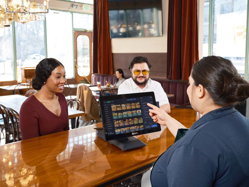 Equipo de restaurante mostrando una pantalla de pedidos y menú digital en mostrador