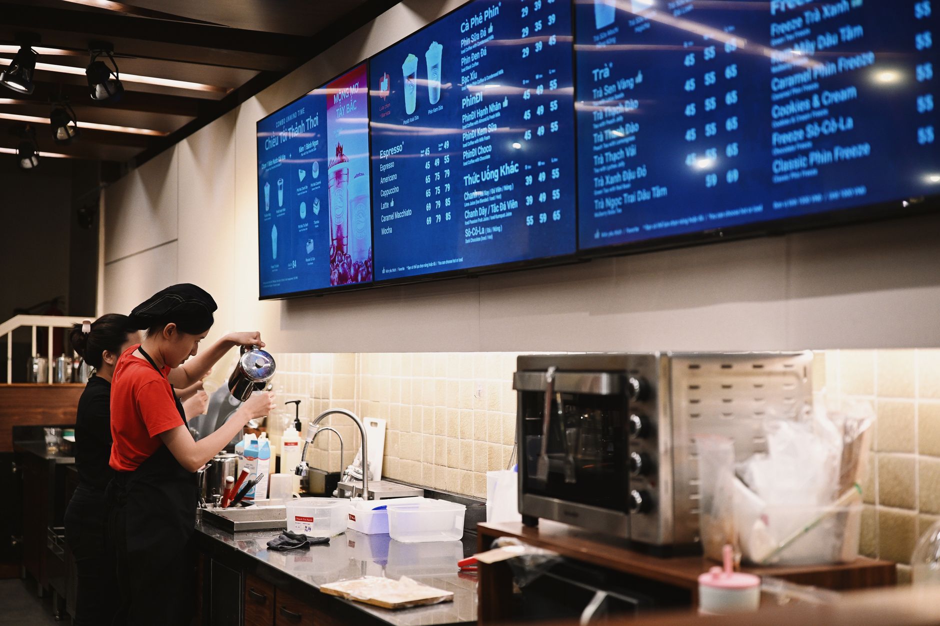 Baristas preparing drinks in a coffee shop with customer-facing screens nearby