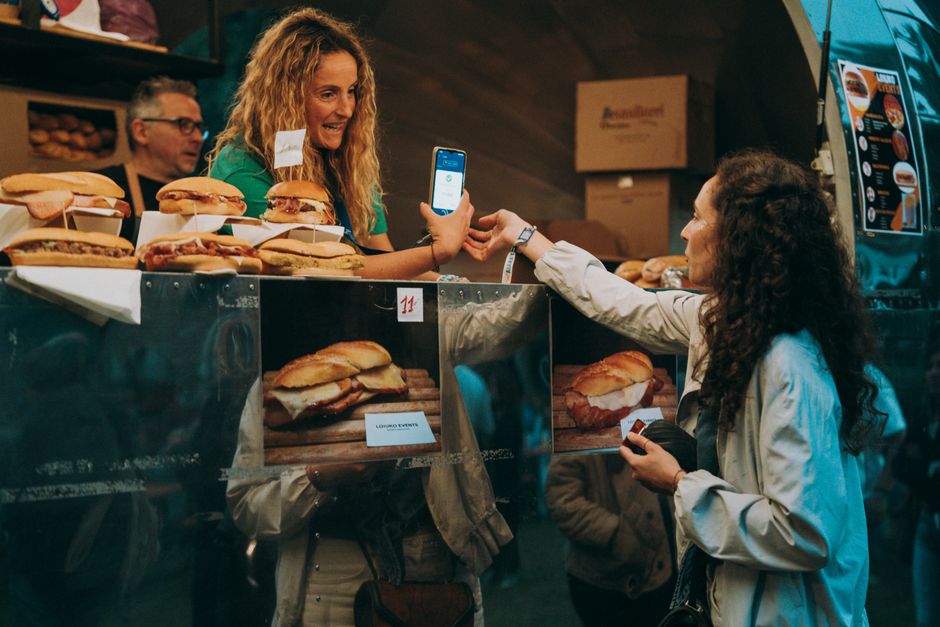 Customer paying by phone at a food truck counter with menu panels visible