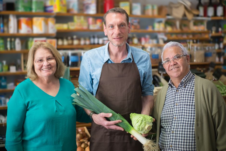 Grocery clerk showing fresh produce to two shoppers at a market counter