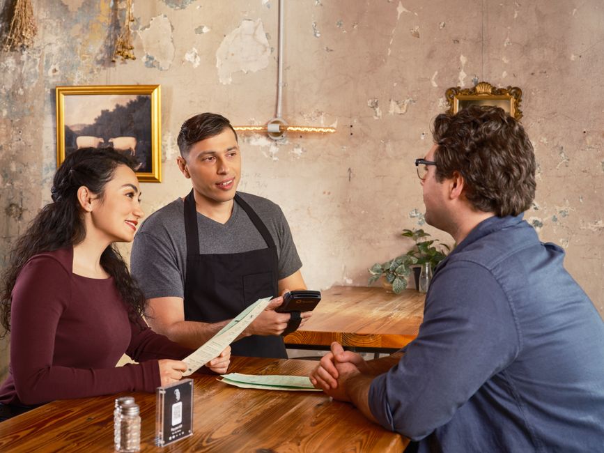 A restaurant server using a handheld POS while helping guests