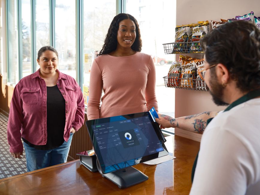 Customers paying at a modern checkout beside a cloud-connected screen
