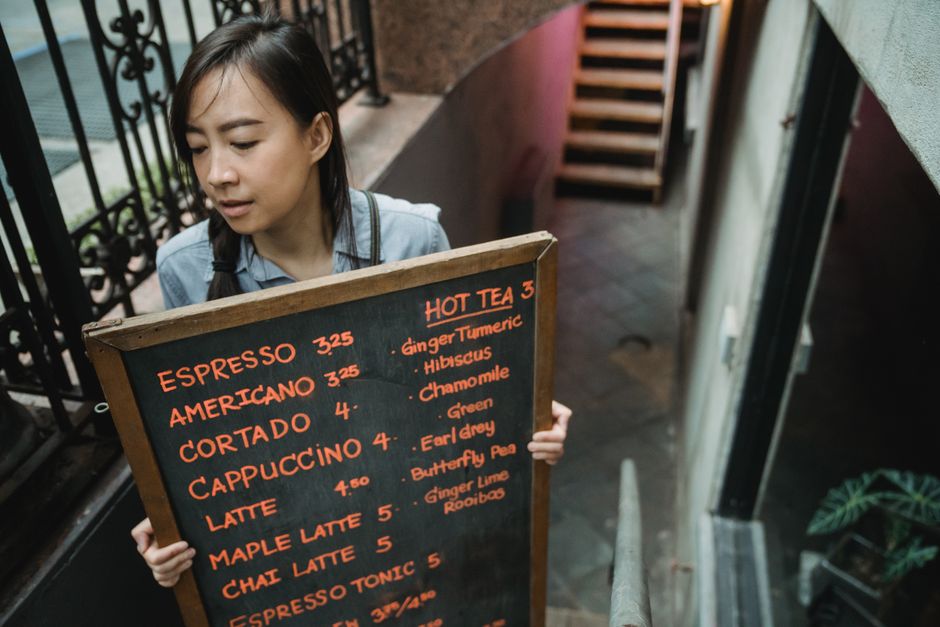 A café operator carrying a chalkboard menu outside