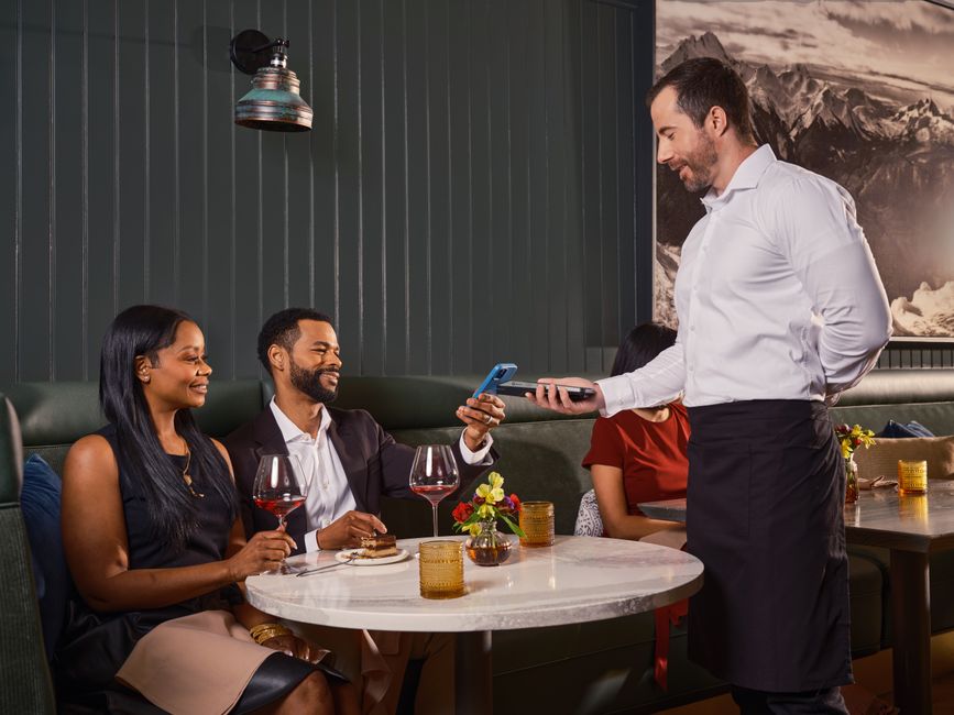 Waiter helping restaurant customers complete a contactless payment